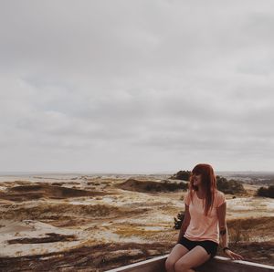 Woman sitting at beach against sky