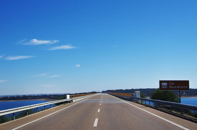 Road leading towards city against blue sky