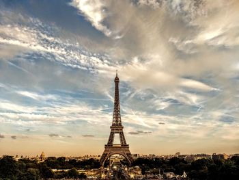 Communications tower in city against cloudy sky