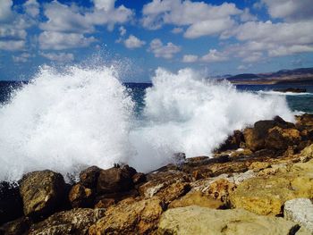 Waves splashing on rocks at shore against sky