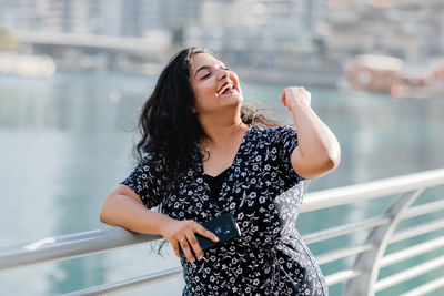 A positive girl smiles while walking along the embankment, laughs and throws her hair back