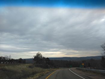 Road passing through landscape against cloudy sky