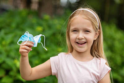 Portrait of smiling girl holding mask while standing outdoors