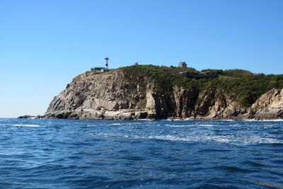 Scenic view of sea by cliff against clear blue sky