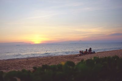 People on beach against sky during sunset