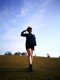 Full length of woman saluting while standing on field against sky