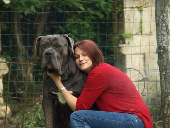 Portrait of woman petting dog while crouching against fence