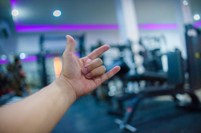 Cropped image of person showing horn sign while standing in gym