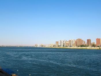 Scenic view of sea and buildings against clear blue sky