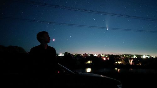 Silhouette man looking at illuminated city against sky at night