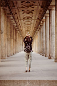 Full length rear view of woman photographing in corridor