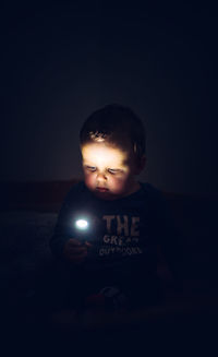 Cute boy holding flashlight sitting outdoors at night