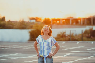 Full length of smiling woman standing against sky during sunset