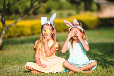 Sisters holding easter eggs while sitting at lawn