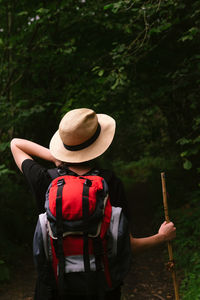 Rear view of man holding hat against trees