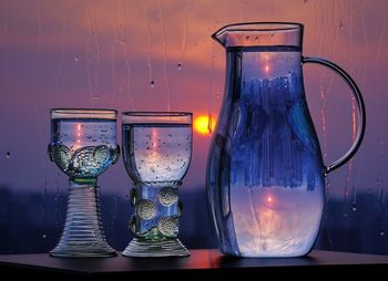 A water jug and drinking glasses containing bubbled water reflecting distant buildings at sunset