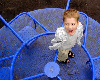High angle view of boy with mouth open standing on blue merry-go-round
