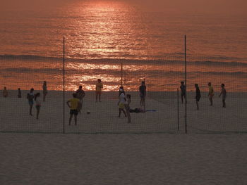 People playing volleyball at beach during sunset