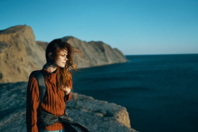 Young woman standing on rock by sea against clear sky