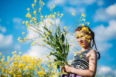 Cute girl holding flower while standing against sky