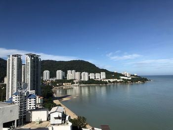 Buildings by sea against blue sky