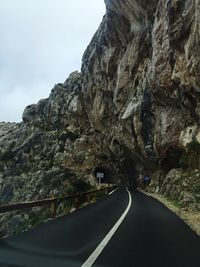 Road leading towards rock formation against sky