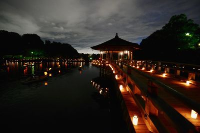 Illuminated lights by sea against sky at night