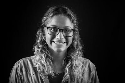 Portrait of smiling young woman against black background