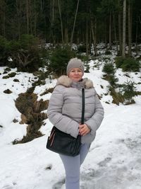 Full length portrait of smiling woman on snow covered trees