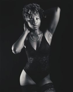 Portrait of young woman standing against black background