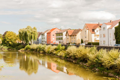 Houses by river and buildings against sky