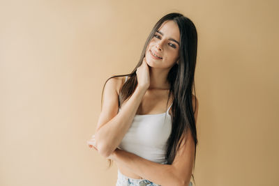 Portrait of young woman standing against yellow background