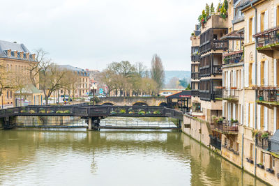 Bridge over river by buildings against sky