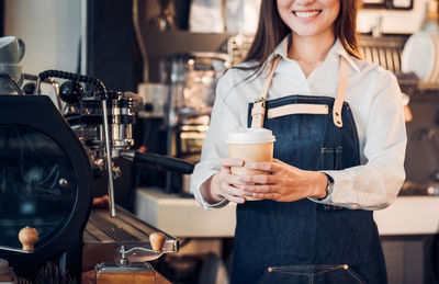 Midsection of smiling barista holding disposable cup in cafe