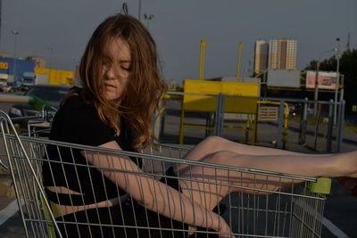 Beautiful young woman sitting in shopping cart on road