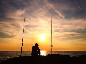 Silhouette man fishing on beach against sky during sunset