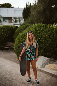 Beautiful young female with a skate board and sunglasses at dusk