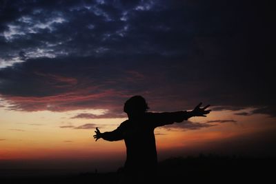 Silhouette man with arms outstretched standing against sky during sunset