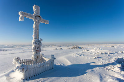 Snow covered cross against blue sky