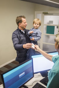 Mature man giving id card to female doctor while carrying son in hospital