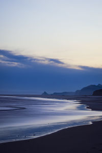 Scenic view of beach against sky at sunset