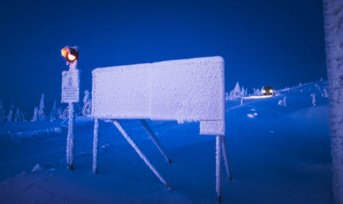 Frozen information sign by road signal on snow covered field at dusk