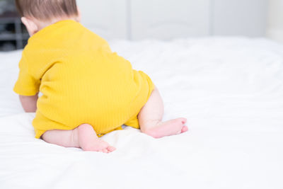 Rear view healthy asian baby girl 5 months in yellow bodysuit on bed on white bedding
