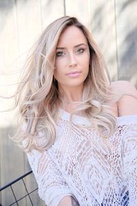 Portrait of beautiful young woman sitting against fence