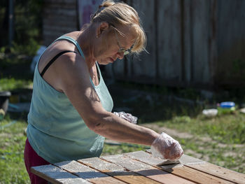 Side view of senior woman painting wooden table in yard