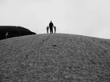 Father with kids on sand at beach against sky