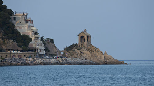 Buildings by sea against clear blue sky