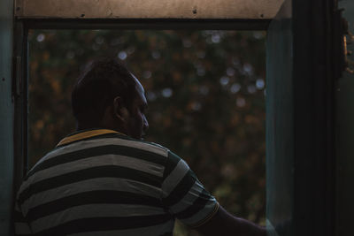 Rear view of man looking through window