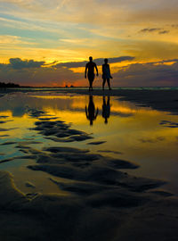 Silhouette people walking at beach against sky during sunset