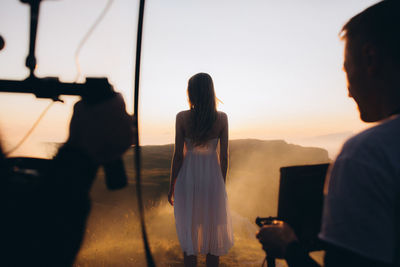 Photographers and model in desert against sky during sunset